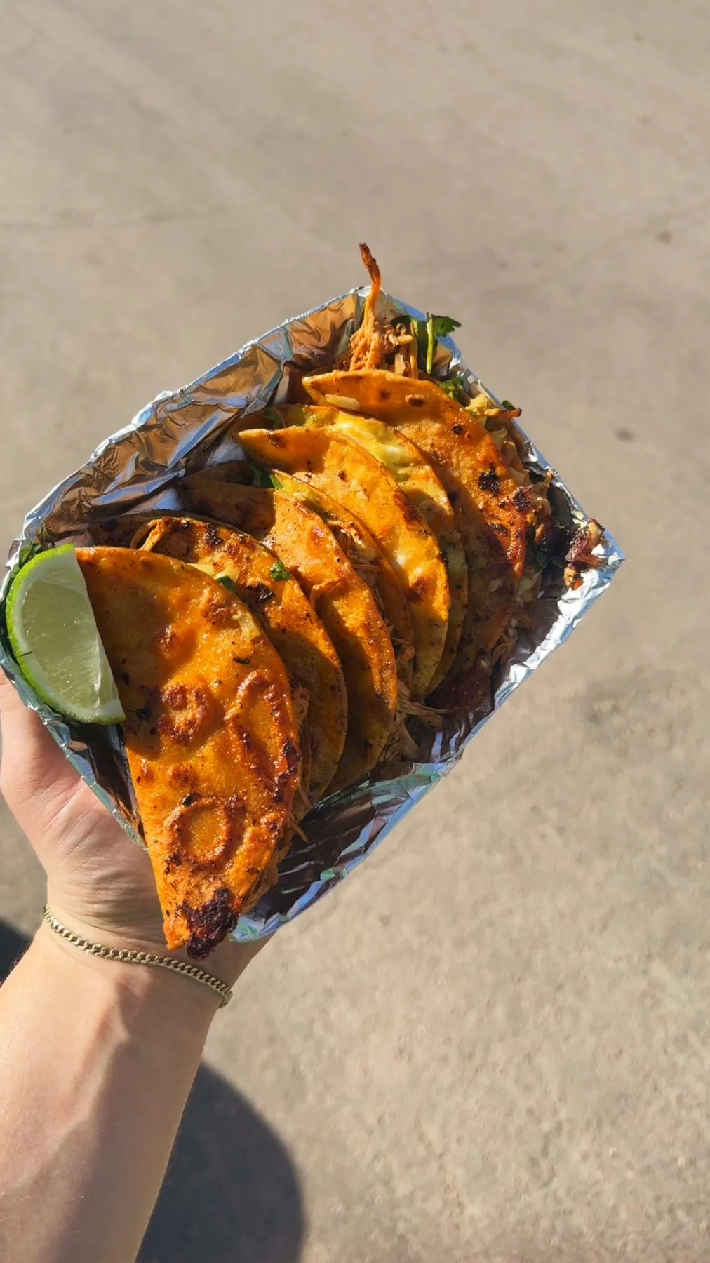 Tray of crispy birria tacos with a lime wedge, held up to the sky